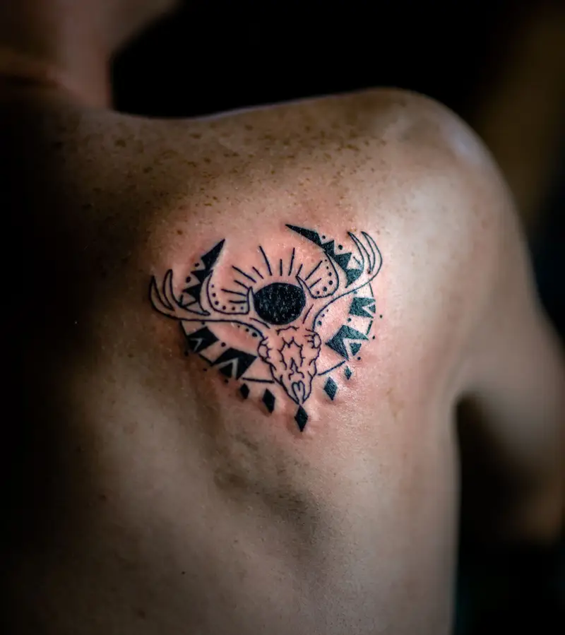 Small black ornamental emblem with a central eye on a shoulder blade
